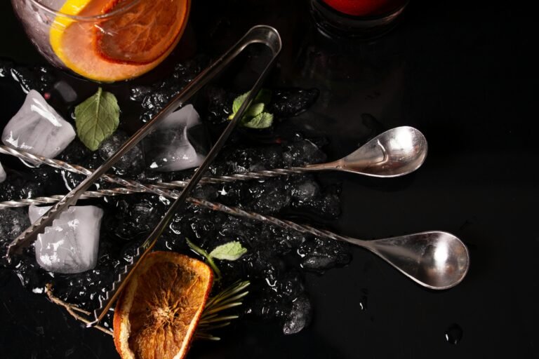 Flatlay showing cocktail ingredients with citrus slices, ice, and bar tools on a dark surface.